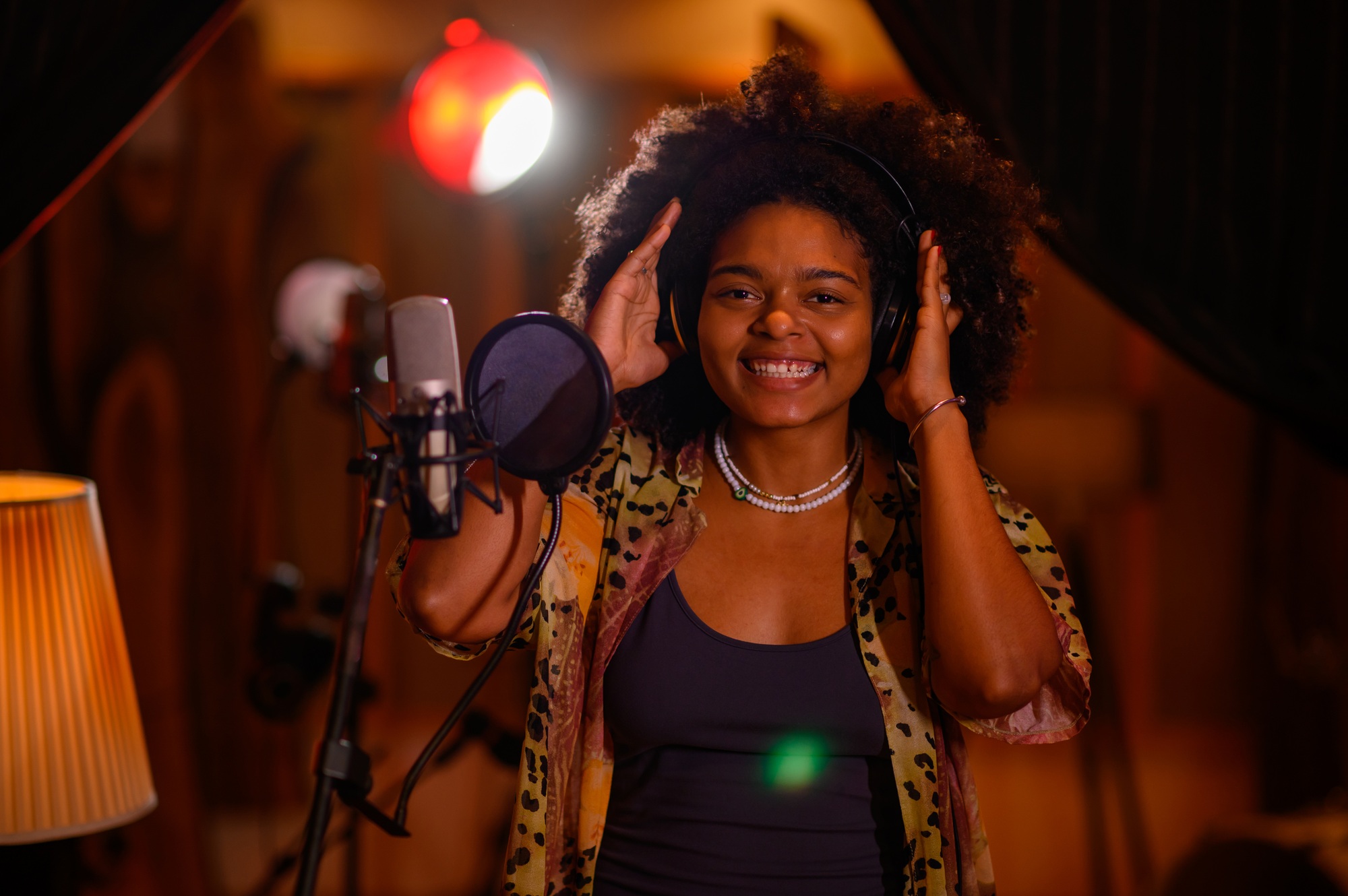 Portrait of a happy multiracial singer with curly hair in a recording studio vocal booth.