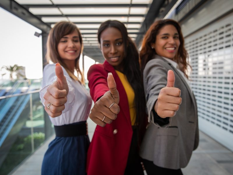 Three businesswomen with thumbs up, expression of satisfaction and approval.